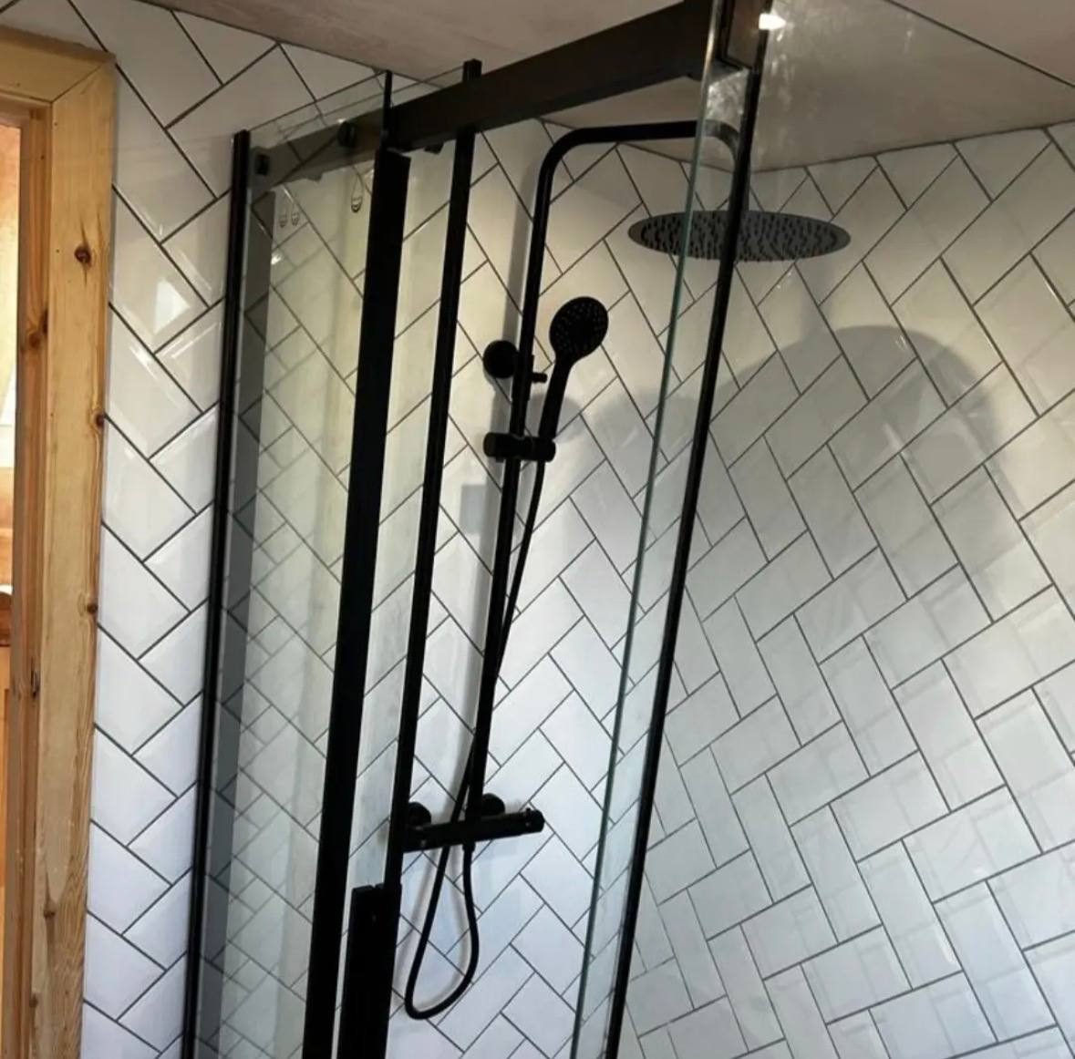 Black rainfall shower and rise rail in a herringbone tiled shower enclosure