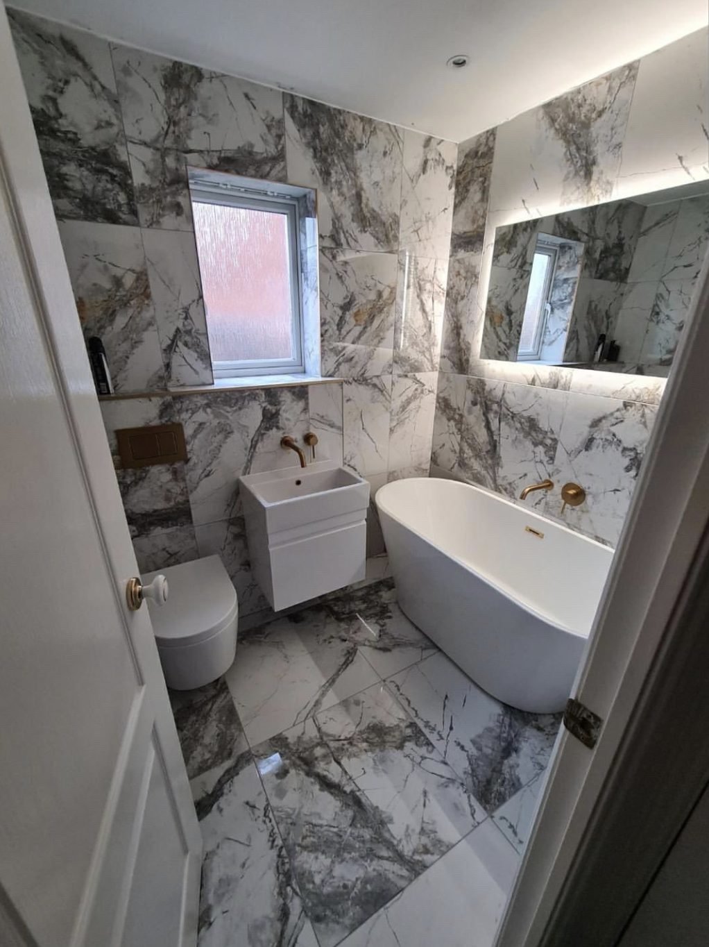 Marble tiled bathroom with freestanding bath, wall hung WC and brushed gold taps